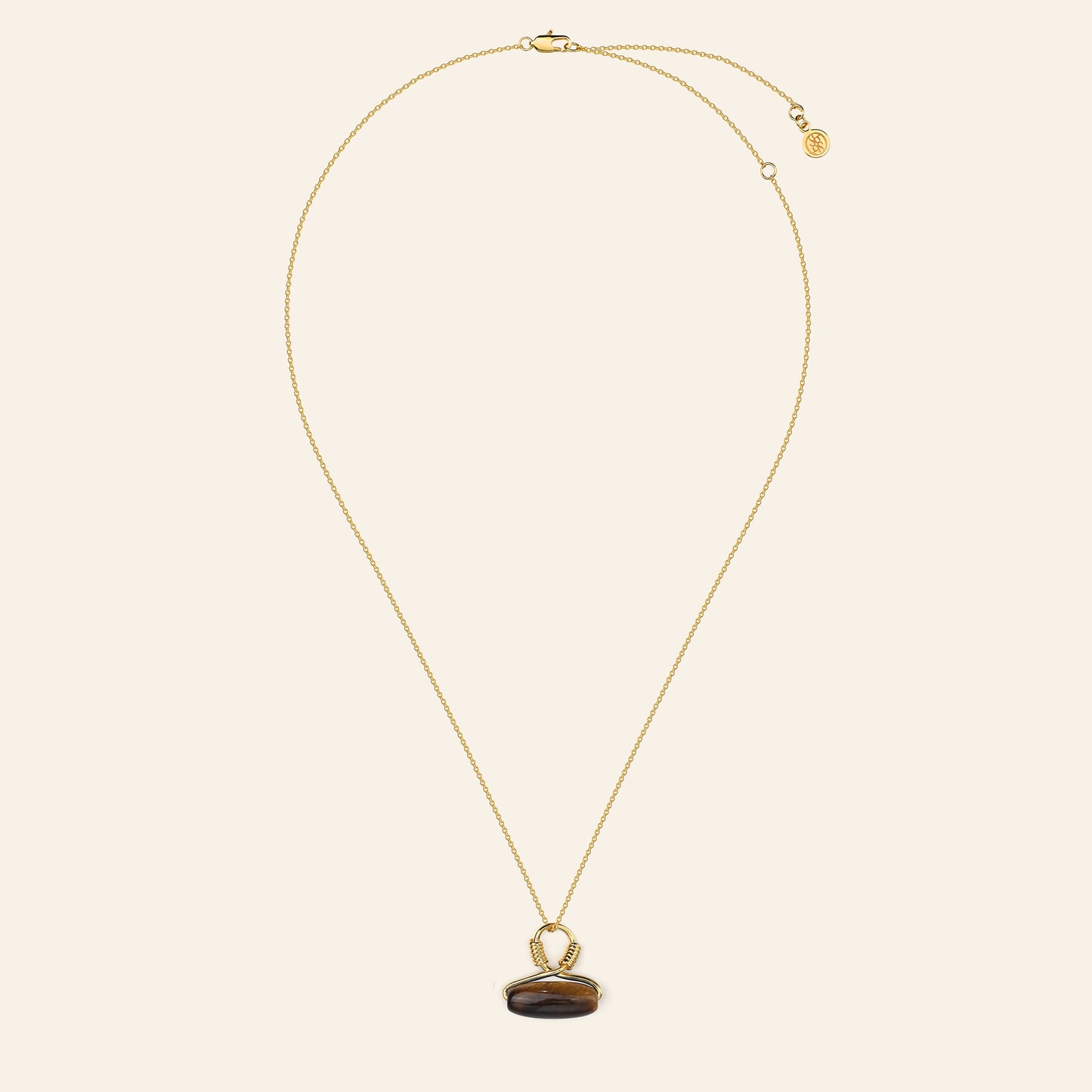 Gold necklace with a tigers eye pendant on a beige background