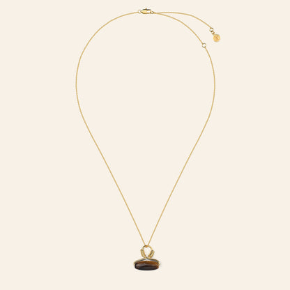 Gold necklace with a tigers eye pendant on a beige background