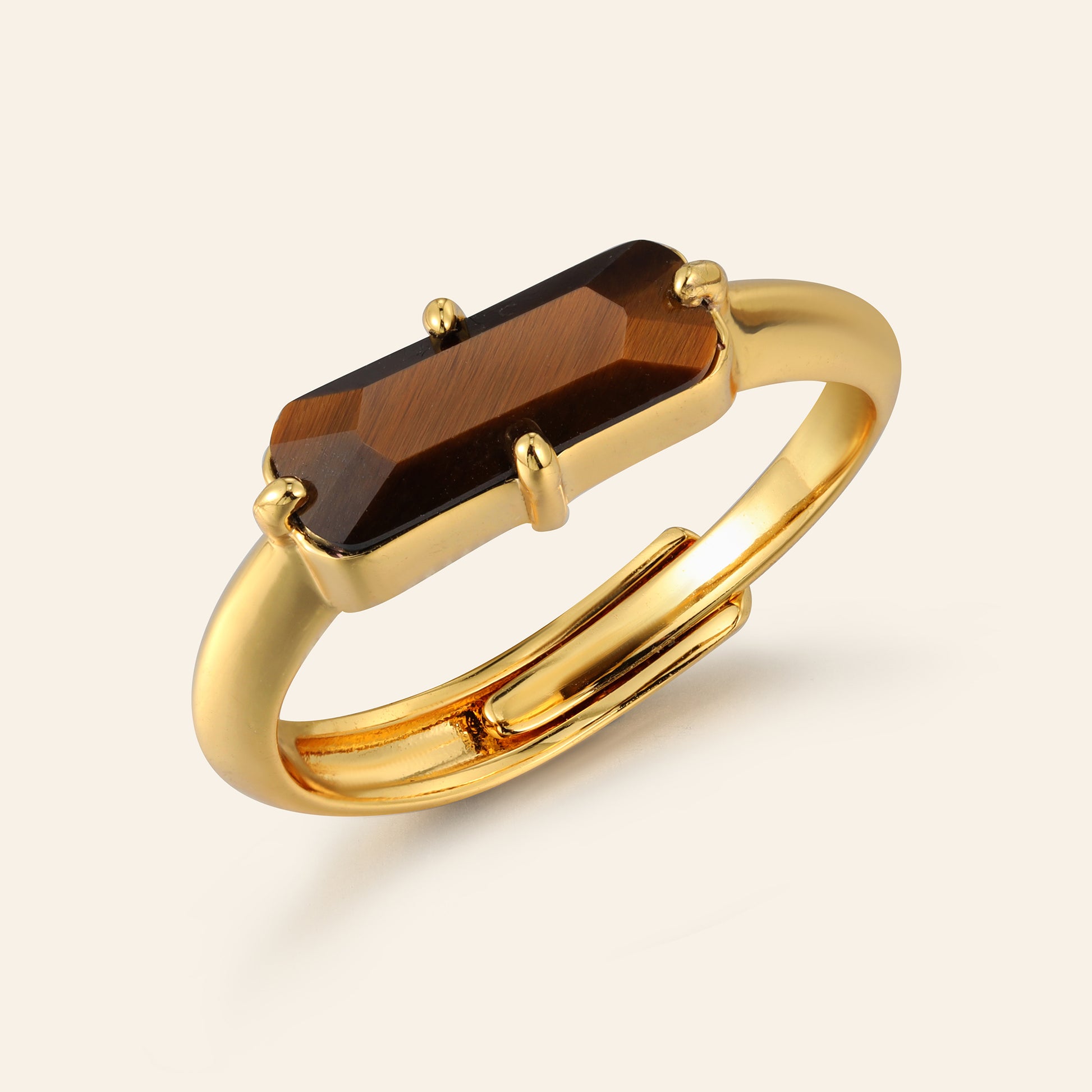 Gold ring with a rectangular tigers eye gemstone on a beige background
