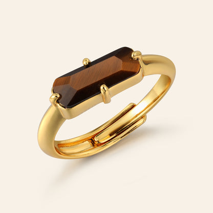 Gold ring with a rectangular tigers eye gemstone on a beige background