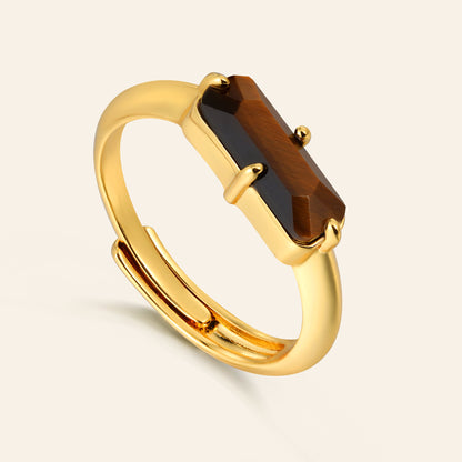 Gold ring with a rectangular tigers eye gemstone on a light beige background