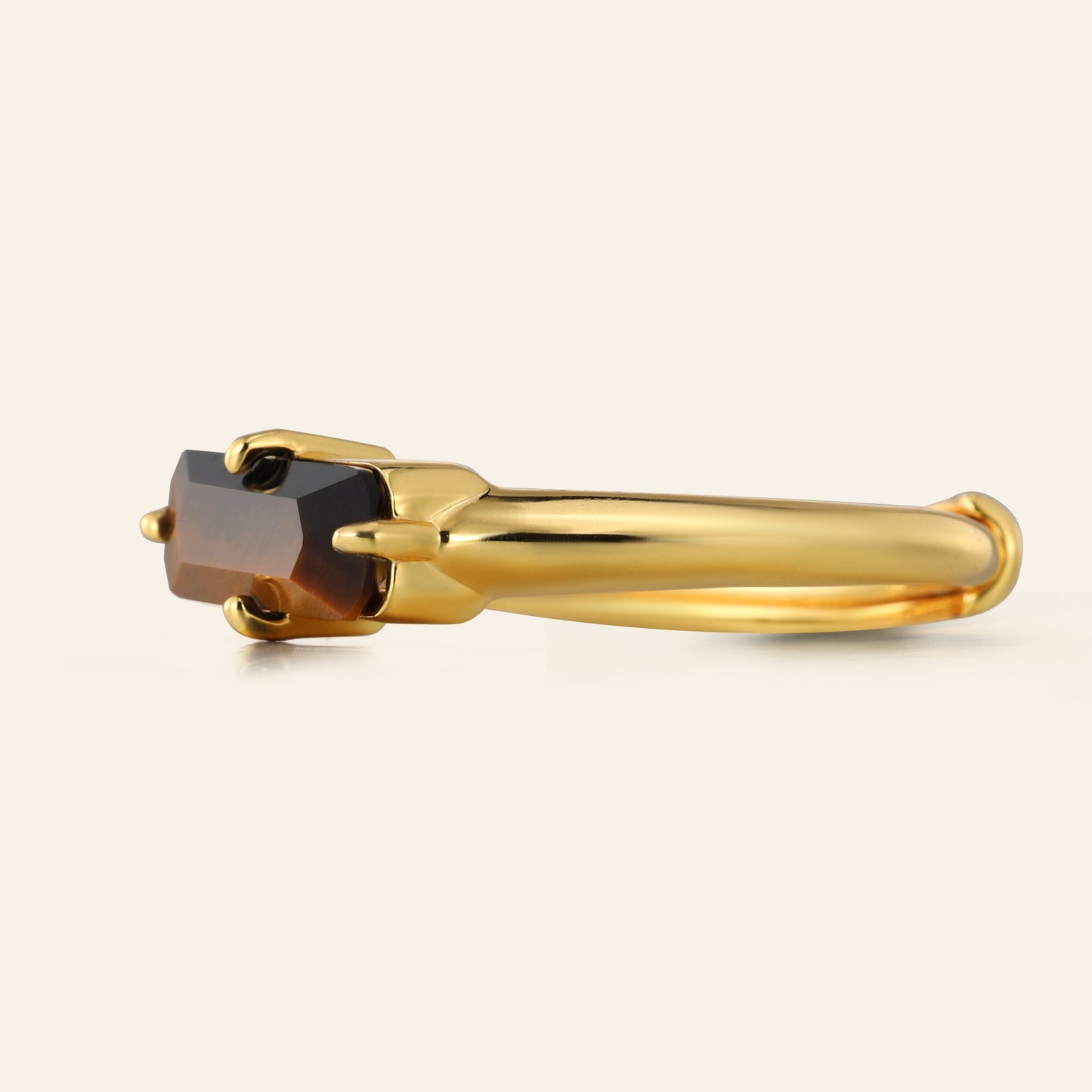 Gold ring with a tigers eye stone on a light beige background