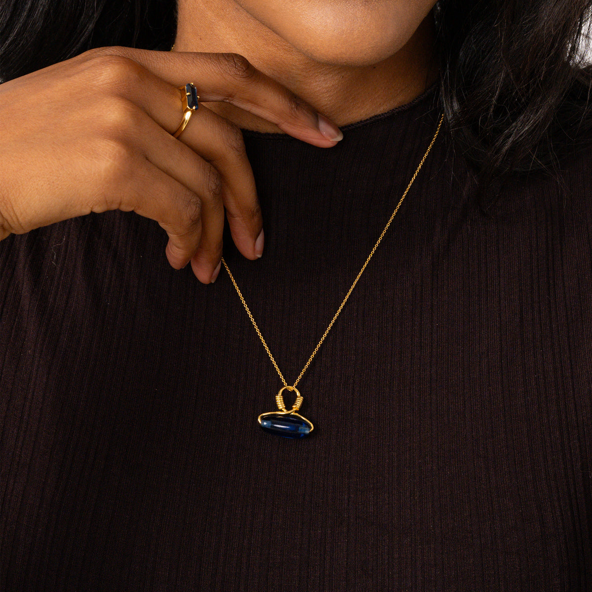 Person wearing a gold necklace with a blue pendant on a dark background