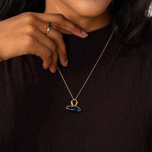 Person wearing a gold necklace with a blue pendant on a dark background
